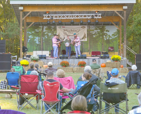 band playing bluegrass music onstage while audience sits outside on lawn chairs watching