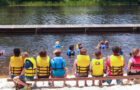 group of campers sitting on a bench in front of the lake