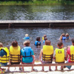 group of campers sitting on a bench in front of the lake