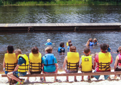 group of campers sitting on a bench in front of the lake