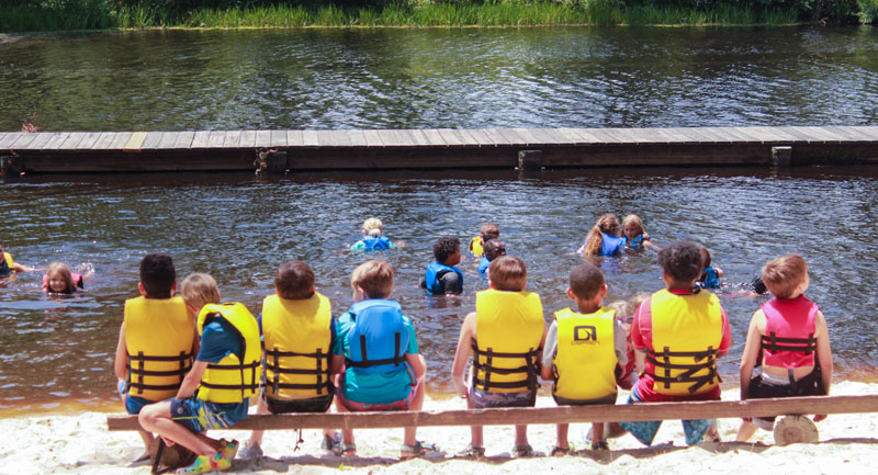 group of campers sitting on a bench in front of the lake